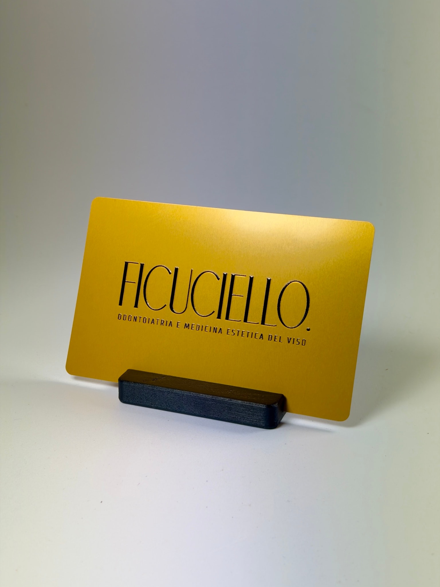 Biglietto da visita in alluminio oro su un supporto nero: il fronte con il logo dello studio stampato in nero con stampa UV