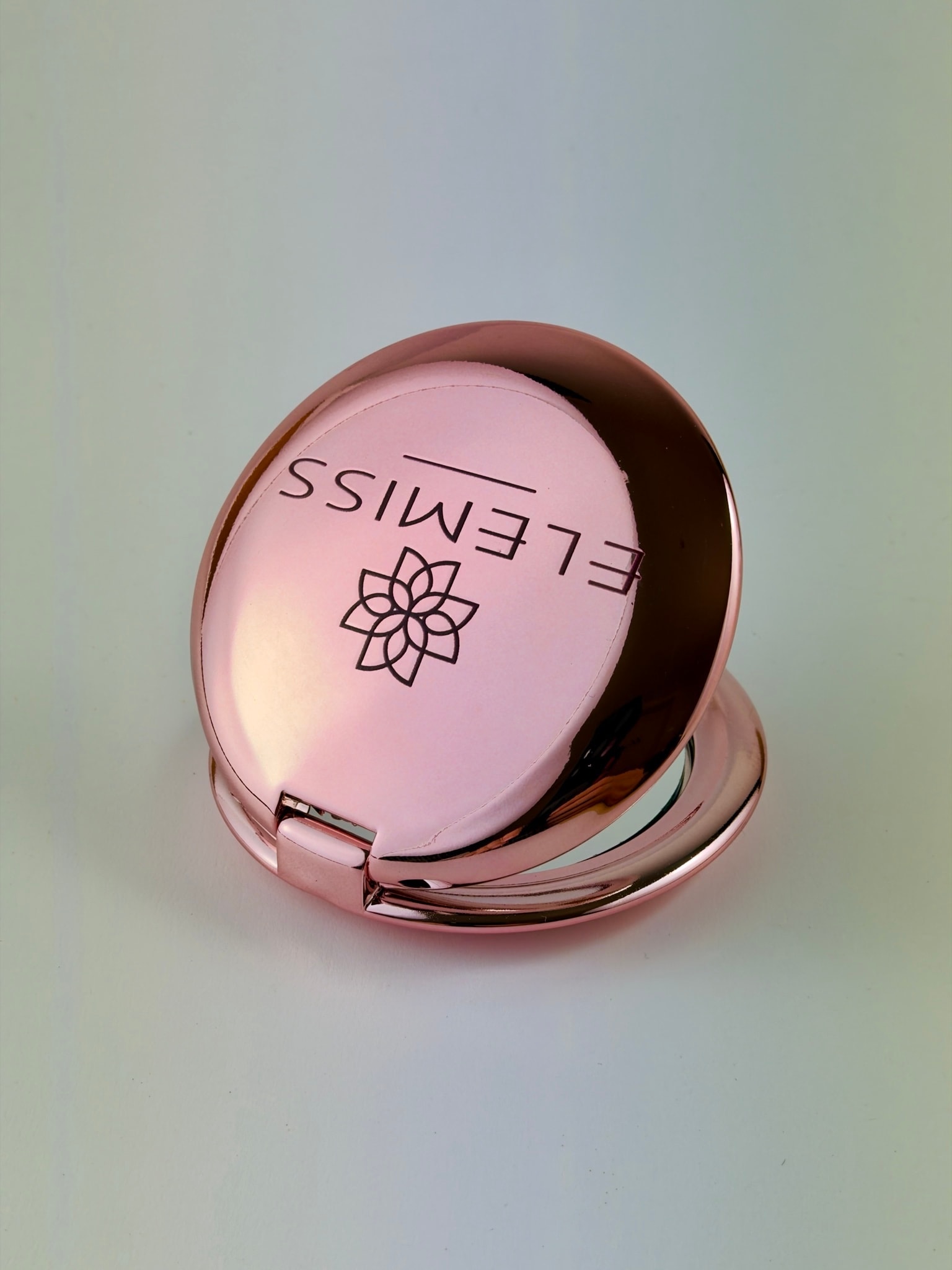 Specchietto rosa aperto con il logo Elemiss, fiore e nome, stampato sul coperchio lucido e curvo